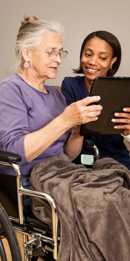 Señora mayor en silla de ruedas con una chica de piel oscura mirando una tableta